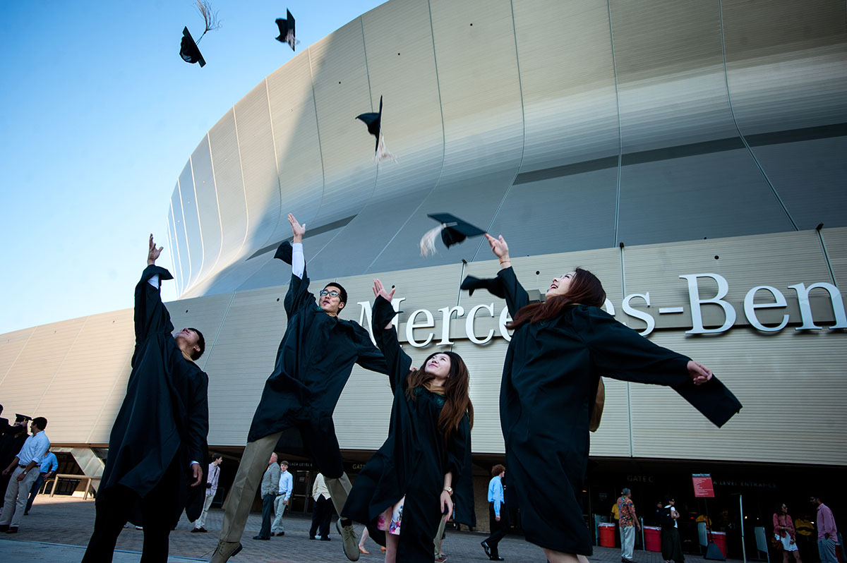 Four students jumping and tossing their graduation caps. 