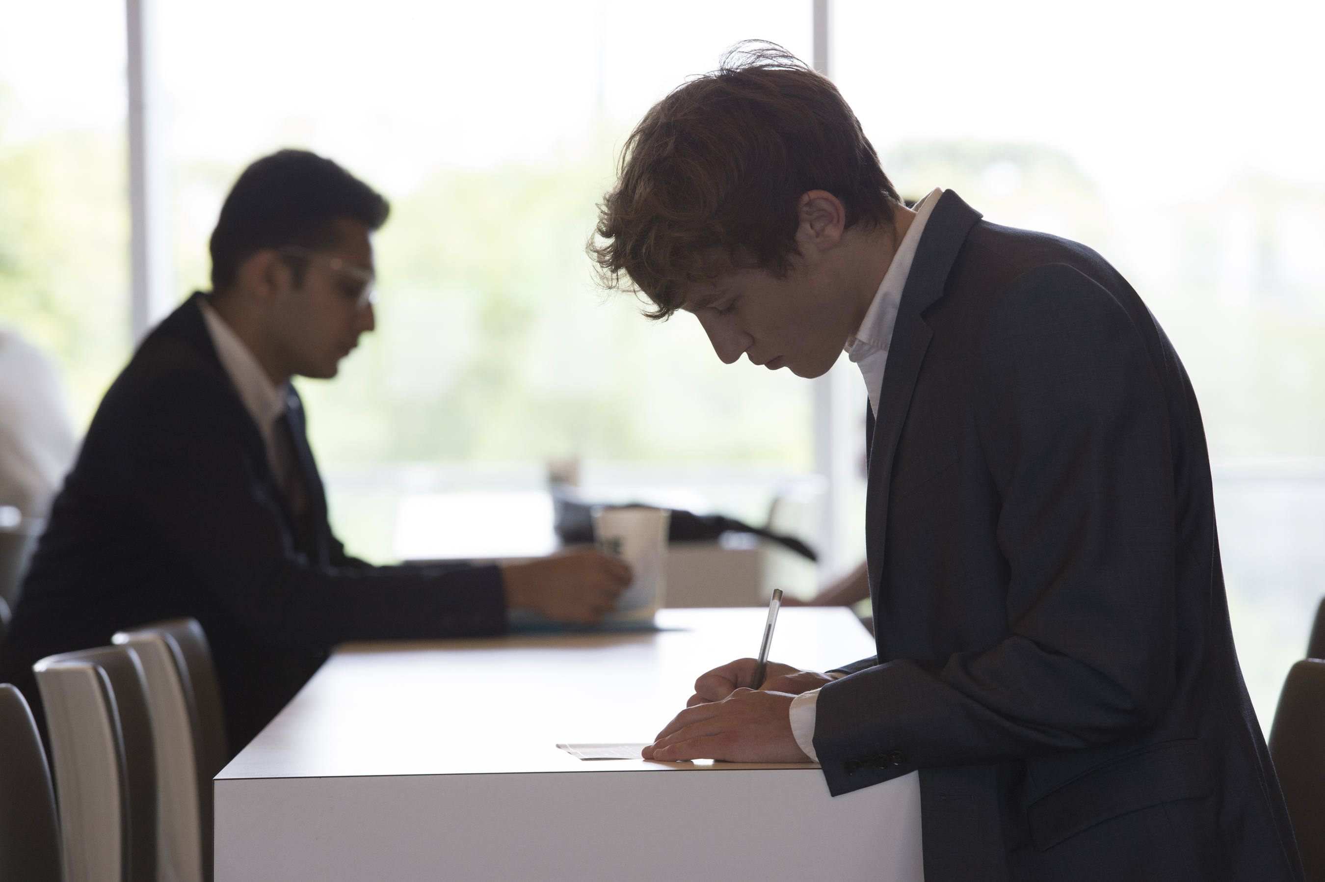 Two students in suits writing notes at a table.